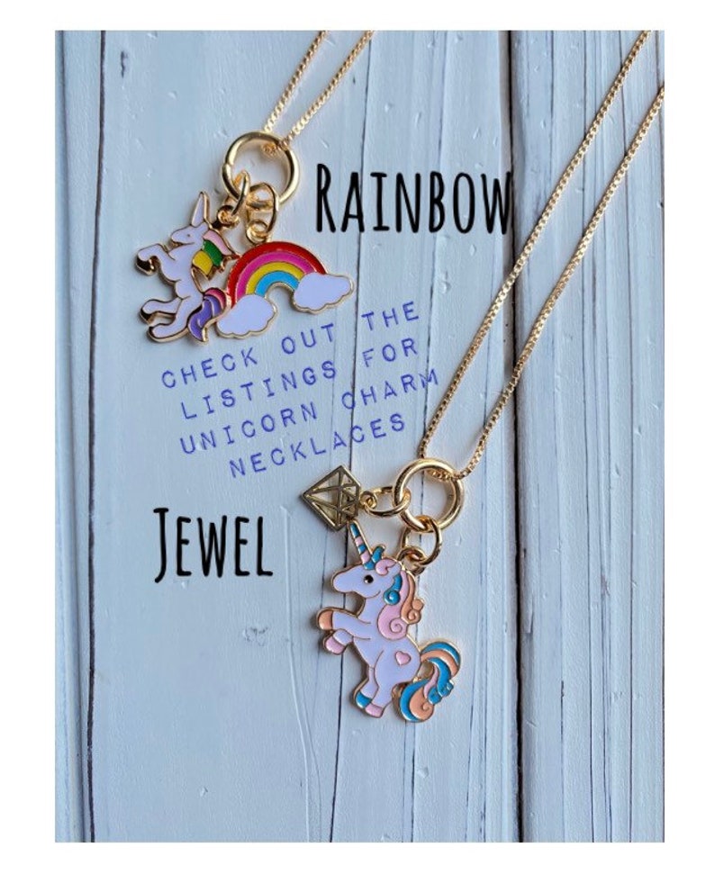 May include: Two gold necklaces with charms. The top necklace has a rainbow and unicorn charm. The bottom necklace has a diamond and unicorn charm. The text "RAINBOW JEWEL" is written on the wooden background. The text "CHECK OUT THE LISTINGS FOR UNICORN CHARM NECKLACES" is also written on the background.