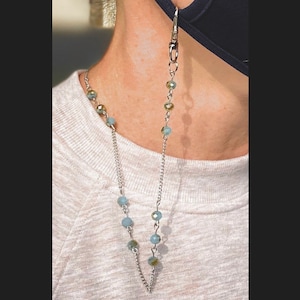 May include: A silver chain with light blue and gold beads, attached to a black face mask. The chain is worn around the neck.