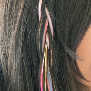 May include: A braided hairstyle with colorful hair extensions and a butterfly-shaped hair clip. The hair extensions are pink, blue, green, yellow, and gold.