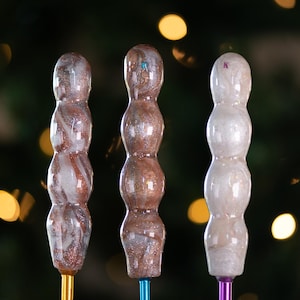 May include: Three crochet hooks with different colored handles. The handles are made of a marbled resin with white and brown swirls. The hooks are made of metal and are attached to the handles.