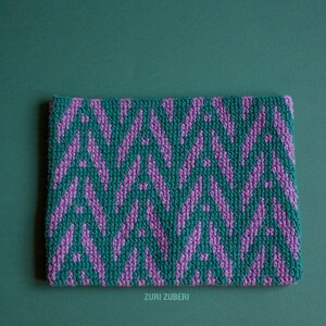 May include: A green and purple crocheted clutch with a geometric pattern. Zuri Zuberri is printed on the bottom.