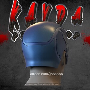 Op de afbeelding: Een blauwe helm met een textuur en een ritsdetail. De helm staat op een grijze achtergrond met rode verfspatten.
