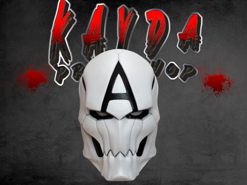 Op de afbeelding: Wit plastic masker met een zwarte letter A aan de voorkant. Het masker heeft een schedelvormig ontwerp met scherpe tanden en een puntige kin.