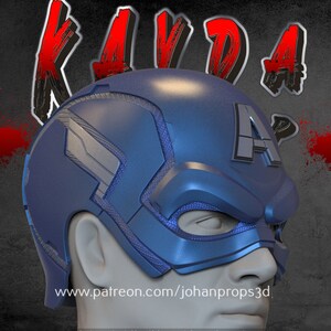 Op de afbeelding: Een blauwe en zilveren Captain America helm met een rode 'A' aan de zijkant. De helm wordt gedragen door een persoon met een wit gezicht. De achtergrond is grijs met rode spatten.
