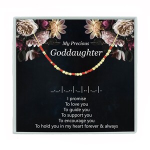 May include: A red and gold beaded bracelet with the words "My Precious Goddaughter" and a message in Morse code that reads "I promise to love you, to guide you, to support you, to encourage you, to hold you in my heart forever & always".