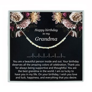 May include: A silver necklace with gold beads and a card that reads "Happy birthday to my Grandma". The card has a floral background with pink and purple flowers.