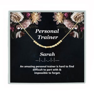 May include: A black gift box with a floral design and gold trim. The box contains a gold necklace with a name spelled out in beads. The text on the box reads "Personal Trainer Sarah ...-..-..-. ...". An amazing personal trainer is hard to find difficult to part with & impossible to forget.