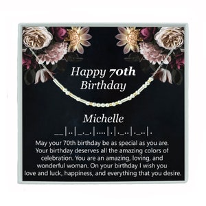 May include: A silver necklace with gold beads and a black box with a floral design. The box has the text "Happy 70th Birthday Michelle" on it.