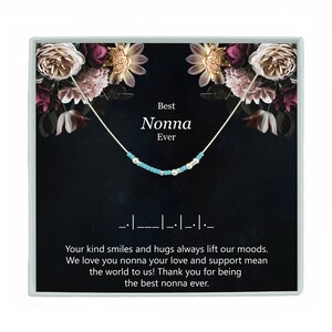 May include: A silver necklace with turquoise and silver beads, displayed in a box with a floral design. The box has the text "Best Nonna Ever" and a message about kind smiles and hugs.