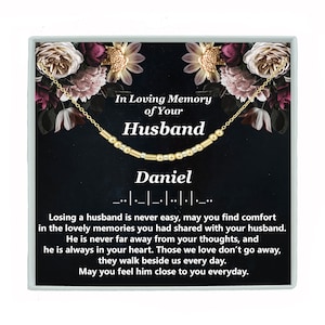 May include: A gold necklace with a message that reads "In Loving Memory of Your Husband Daniel" and a quote about losing a loved one. The necklace is displayed in a black box with a floral design.