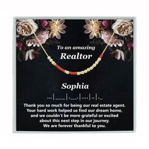 May include: A black and gold gift box with a floral design and a red and gold beaded necklace. The box has a message that reads "To an amazing Realtor Sophia" and a thank you message for the realtor.