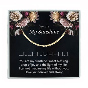 May include: A black and gold necklace with a floral design on the box. The necklace has gold beads and a message that reads "You are my sunshine, sweet blessing, drop of joy and the light of my life. I cannot imagine my life without you. I love you forever and always."