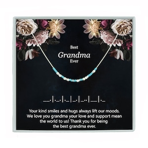 May include: A silver necklace with blue beads and a card that reads "Best Grandma Ever". The card has a floral background and the text "Your kind smiles and hugs always lift our moods. We love you grandma your love and support mean the world to us! Thank you for being the best grandma ever."
