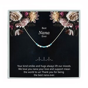 May include: A silver necklace with turquoise beads and a silver charm that says "Best Nana Ever". The necklace is displayed in a black box with a floral design and a message that reads "Your kind smiles and hugs always lift our moods. We love you nana your love and support mean the world to us! Thank you for being the best nana ever."