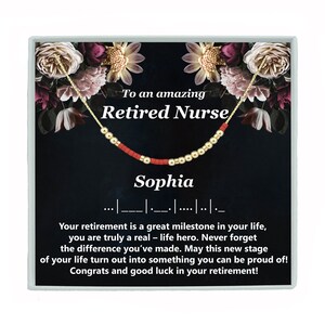 May include: A gold necklace with red beads and the words "To an amazing Retired Nurse Sophia" on a black background with floral accents.