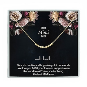 May include: A gold necklace with a bar and bead design in a black box with a floral pattern. The box has the text "Best Mimi Ever" and "Your kind smiles and hugs always lift our moods. We love you Mimi your love and support mean the world to us! Thank you for being the best Mimi ever."