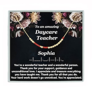 May include: A gift box with a floral design and a gold necklace with red beads. The box has a message that reads "To an amazing Daycare Teacher Sophia".