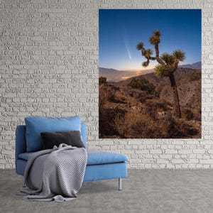 May include: A lone Joshua tree stands tall against a twilight sky, with a bright comet streaking across the horizon. The scene is framed by a distant mountain range and a vast desert landscape.