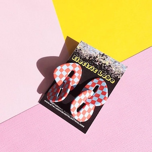 May include: A pair of red and blue checkered hair clips with the text "Electric Lobe" and website information on a black card.