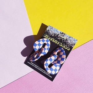 May include: A pair of blue and white checkered earrings in the shape of the number 9. The earrings are on a card that says "Electric Lobe" and includes the shop's Instagram and Etsy links.