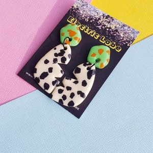 May include: A pair of green and orange patterned earrings with a white and black animal print design. The earrings are on a black card with the text "Electric Lobe".