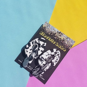 May include: A pair of black and white patterned earrings with a unique shape. The earrings are on a black card with the text "Electric Lobe" and a website address.