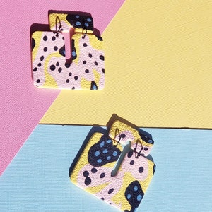 May include: A pair of yellow, pink and black abstract patterned earrings. The earrings are made of polymer clay and have a unique, modern design.