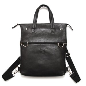 May include: A black leather convertible bag with a pebbled texture, featuring two top handles, a horizontal zippered compartment, silver-toned hardware, and adjustable black fabric shoulder straps. An embossed X logo is centered on the front.