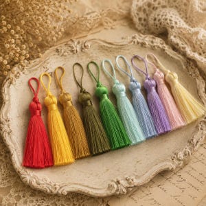 Può includere: Una collezione di nappe colorate in varie tonalità, tra cui rosso, giallo, verde e blu. Ogni nappa è realizzata con fili morbidi e setosi e ha un anello per appenderla. Le nappe sono disposte su un vassoio decorativo bianco sporco.