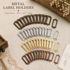 May include: Metal label holders in antique bronze, silver, gold, and copper. The rectangular frames have a decorative top. The image includes the text "METAL LABEL HOLDERS" and the colors of the label holders.