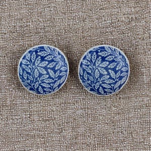 Op de afbeelding: Een paar blauwe en witte keramische oorbellen met een bladmotief.