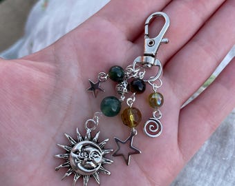 May include: A silver keychain with a sun and moon charm, star charms, and various colored beads. The sun charm has a smiling face. The keychain is attached to a silver clasp.