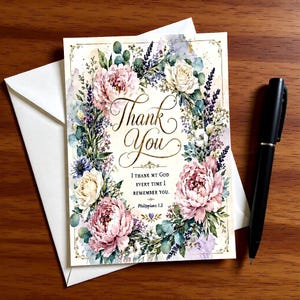 May include: A rectangular greeting card featuring a floral wreath of pink peonies, white roses, and lavender sprigs. The text reads Thank You, I thank my God every time I remember you, and Philippians 1:3. A black pen rests beside the card and envelope.