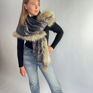 May include: A woman wearing a black turtleneck top and blue jeans with a floral patterned scarf with a faux fur trim.