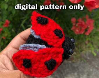May include: A crocheted ladybug amigurumi toy with red and black accents. The ladybug is in a curled up position with its wings folded. The toy is held in a hand.