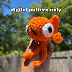 Pode incluir: Um peixe laranja de crochê com olhos brancos e pupilas pretas. O peixe tem barbatanas e pernas. O texto "digital pattern only" está acima do peixe. O nome do artista, "@jfs.art", está na imagem.