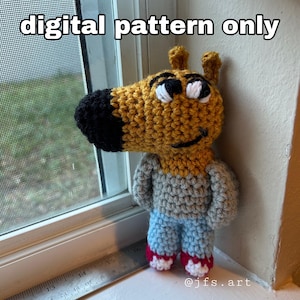 May include: A crocheted plush toy of a cartoon dog wearing a grey sweater and blue jeans. The toy is standing on a windowsill with a ruler in the foreground. The text "digital pattern only" is at the top of the image and "@jfs.art" is at the bottom.