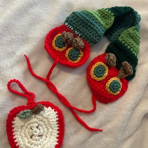 Peut inclure: Ornements crochetés en forme de chenille et de pomme. La chenille est rouge, verte et marron, avec des détails jaunes et verts. La pomme est rouge avec un centre blanc et une feuille verte. Décorations faites à la main.