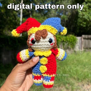 May include: A crocheted jester doll featuring a red and blue hat with yellow accents, a cream-colored face, brown hair, and a red, blue, and yellow body with yellow buttons. The text "digital pattern only" and "@jfs.art" are visible.