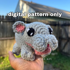 May include: A gray crocheted hippopotamus with pink ears and a pink tongue. The hippopotamus is being held in a person's hand. The text "digital pattern only" is at the top of the image. The text "@jfs.art" is at the bottom of the image.
