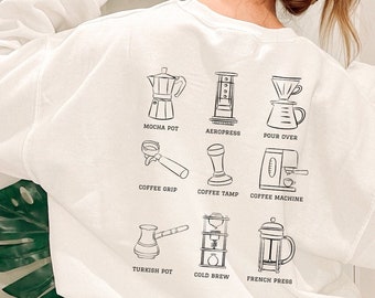 Op de afbeelding: Wit sweatshirt met zwarte lijntekeningen van koffiezetapparatuur, waaronder een mokapot en een cafetière. Tekstlabels identificeren elk item. Een casual, comfortabel kledingstuk.