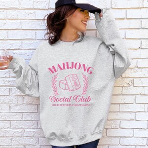 May include: Gray sweatshirt with a pink graphic design that says "Mahjong Social Club" and "Life is better playing Mahjong".
