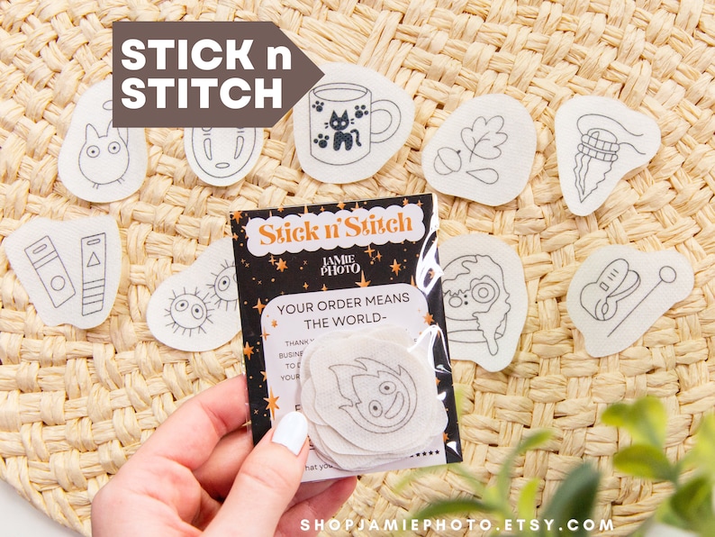 May include: A set of iron-on patches featuring various illustrations, including a cat in a mug, a leaf, a spiral, a Totoro character, a No Face character, a Spirited Away character, and a guitar. The patches are on a woven straw background. The text "Stick n' Stitch" and "Your order means the world" is on a black background with gold stars.