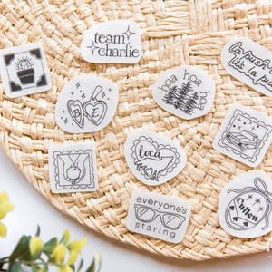 May include: A collection of ten white stickers with black line art designs, including text like team charlie, la push baby, it's la push, loca, everyone's staring, and cullen, alongside illustrations of a cactus, locket, trees, car, apple, and glasses.
