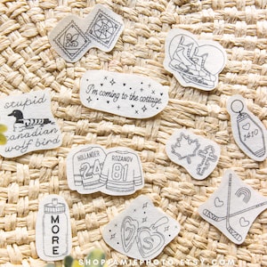 May include: A collection of white stickers with black line art designs including a duck with text, ice skates, a motel keychain, hockey jerseys with numbers 24 and 81, a maple leaf, a cross, a water bottle, and crossed hockey sticks.