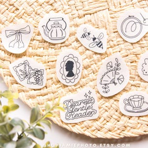 May include: A collection of ten white stickers with black line art illustrations including a bow, a teapot, two bees, an embroidery hoop, two postage stamps, a silhouette portrait, a fan with flowers, a tree, a teacup, and text reading Dearest Gentle Reader.
