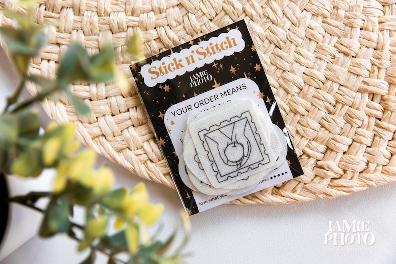 May include: A stack of white Stick n' Stitch embroidery stabilizer sheets featuring a black line art design of hands holding an apple inside a postage stamp border, packaged on a black card with gold stars and the text Stick n' Stitch.