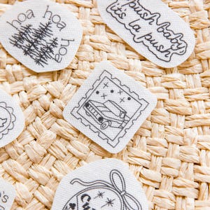 May include: Four white fabric patches with black embroidered designs. One reads 'La push baby it's la push', one features a tree with 'hoa' text, one shows a car in a postage stamp frame, and one is a crest with 'Cullen' and stars.