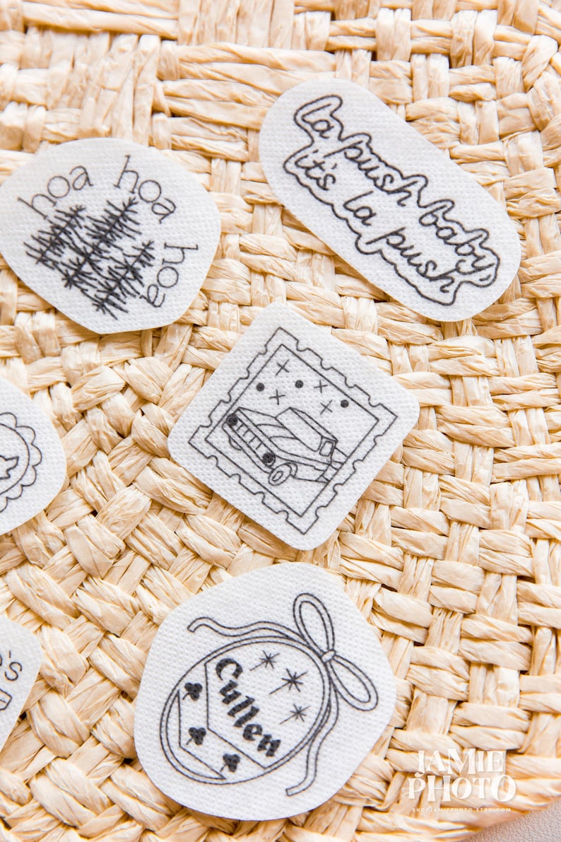 May include: Four white fabric patches with black embroidered designs. One reads 'La push baby it's la push', one features a tree with 'hoa' text, one shows a car in a postage stamp frame, and one is a crest with 'Cullen' and stars.