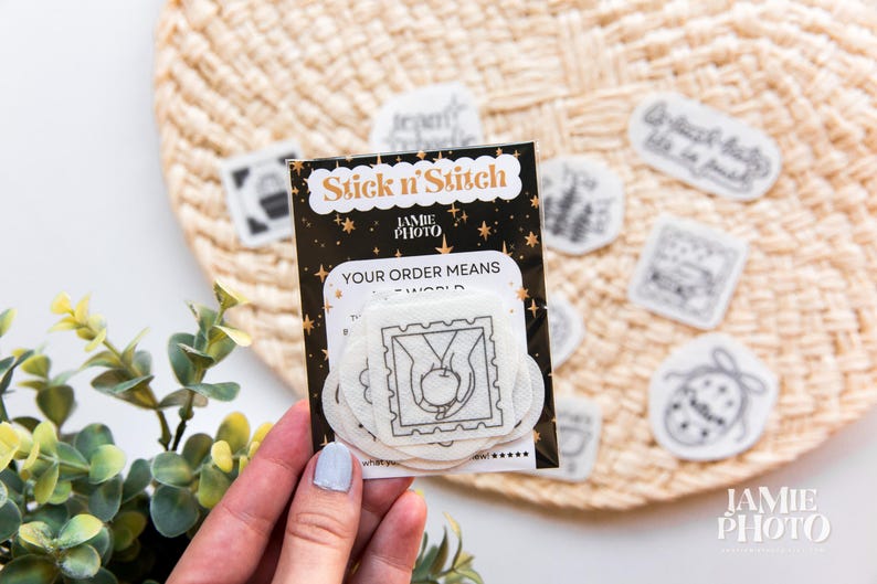 May include: A black and white Stick n'Stitch embroidery stabilizer pack featuring a central square patch with a line art illustration of hands holding an apple. The packaging includes gold star accents and the text Jamie Photo.